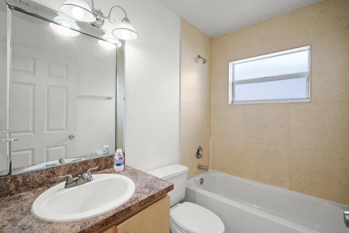 Bathroom featuring a vanity with an integrated sink, a large wall-mounted mirror, a two-bulb vanity light fixture, a toilet, and a bathtub with tile surround