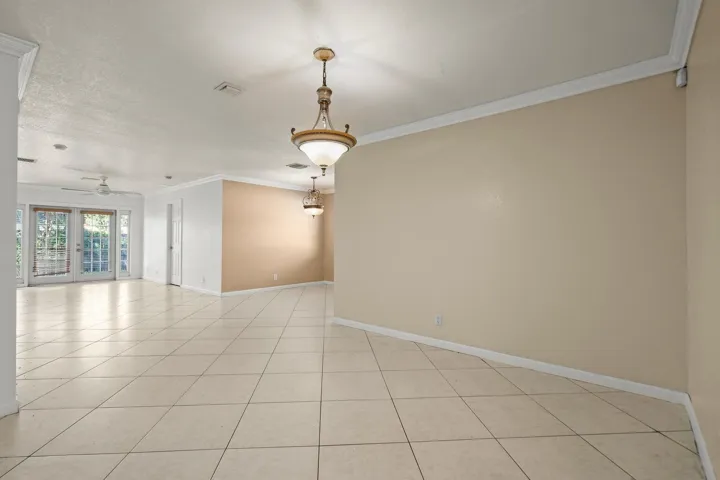 Open-concept interior featuring large format tile flooring, crown molding, and dual French doors