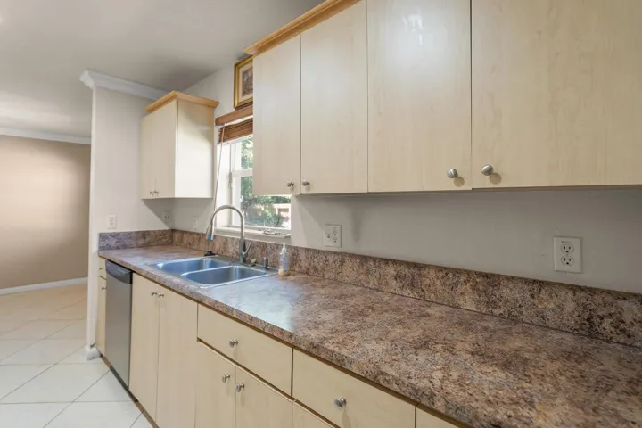 Wood-finish cabinetry, stone-look countertops, stainless steel dual basin sink with a gooseneck faucet, and tiled​​‌​​​​‌​​‌‌​‌‌​​​‌‌​‌​‌​‌​​​‌​​ flooring