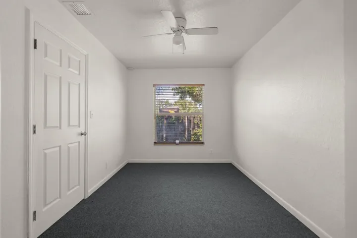White paneled door with brushed nickel hardware, neutral wall finish, window with blinds, ceiling fan, and dark carpet