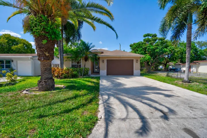 Single-story stucco exterior with an attached garage, paved driveway, and mature palm trees
