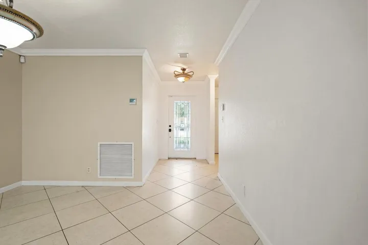 White ceramic tile flooring, crown molding, ceiling-mounted light fixtures, and a glass-paneled entry door