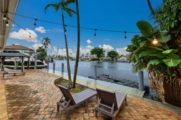 Waterfront property featuring a brick paver patio, mature palm trees, and a private dock