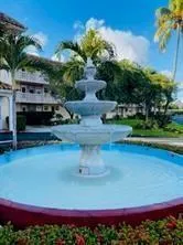Multi-tiered outdoor fountain with a circular basin, surrounded by landscaping and mature palm trees