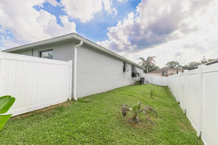 Rear exterior featuring stucco finish, white vinyl fencing, and a manicured lawn