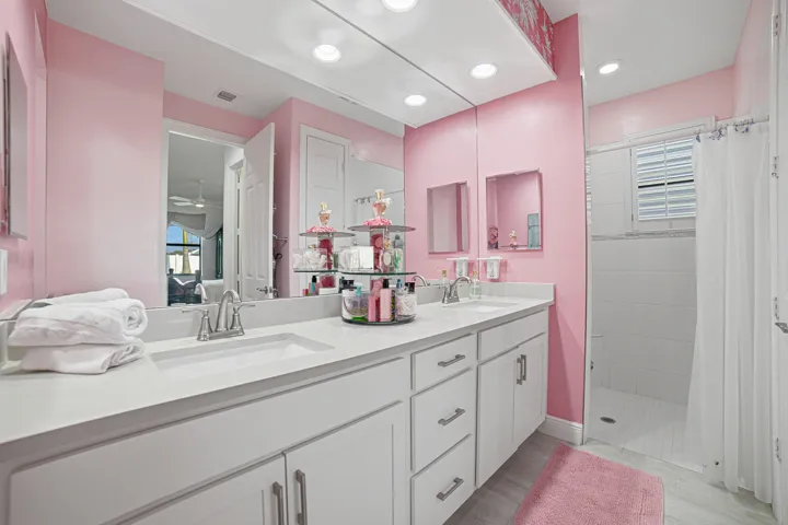 Dual vanity with undermount sinks, white cabinetry, chrome fixtures, and a tiled shower with window
