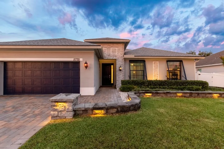 Stucco exterior with stone accents, paver driveway, well-maintained lawn, and established landscaping
