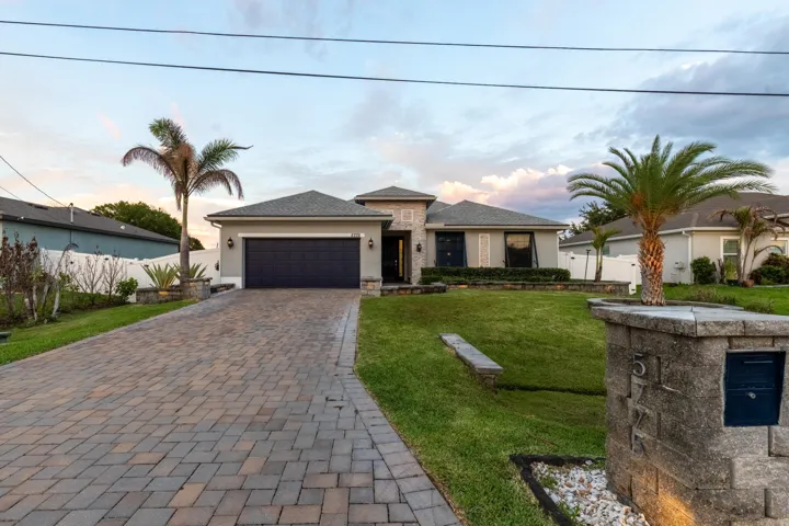 Paver driveway, attached two-car garage, stucco exterior, stone accents, and mature palm trees