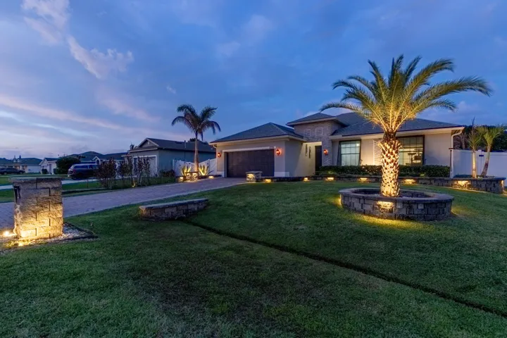 Paver driveway with stone mailbox column, mature palm trees, and stone-clad landscaping features