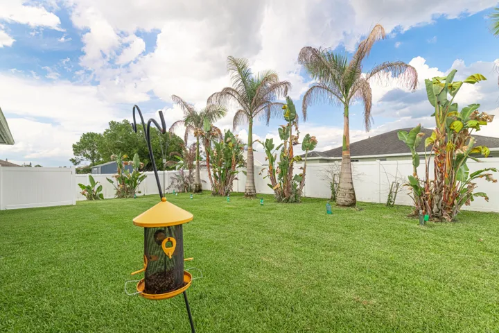 Expansive green lawn, mature palm trees, tropical plantings, and white privacy fencing