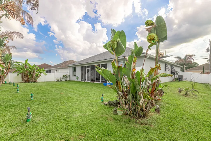 Expansive green lawn, white privacy fencing, and tropical landscaping