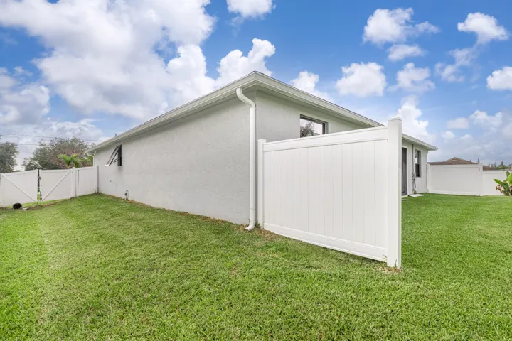 Expansive grassy yard with white privacy fencing and a stucco exterior