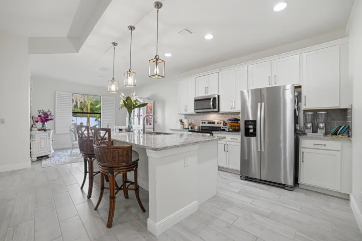 Kitchen featuring white cabinetry, stainless steel appliances, a center island with a stone countertop, pendant lighting, and light wood-finish flooring