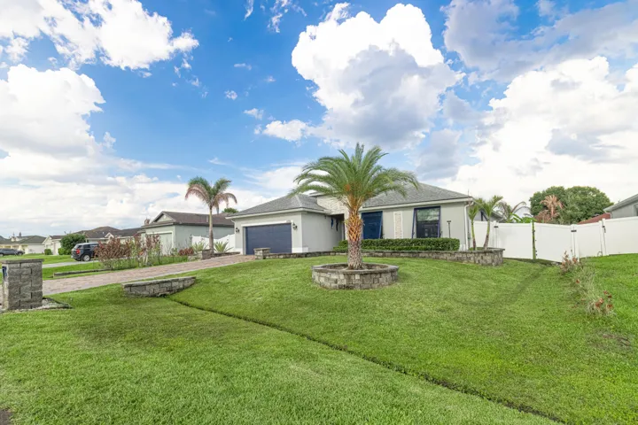 Single-story residence with a gray exterior, a paved driveway, an attached garage, a white privacy fence, and mature landscaping