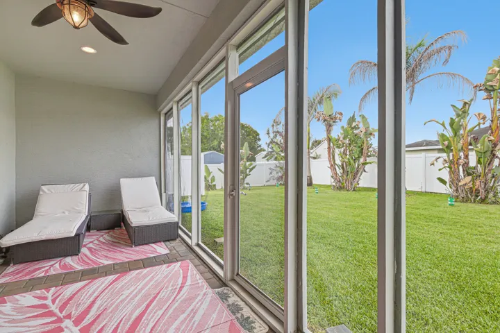 Screened patio with paver flooring, overhead ceiling fan, recessed lighting, and full-length windows overlooking a fenced backyard with mature landscaping