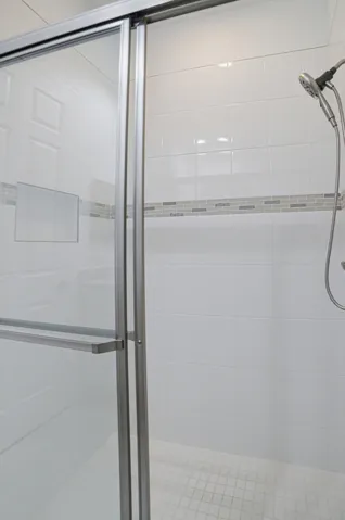 Sliding glass shower enclosure with white tiled walls, decorative accent tile band, and a mosaic tile shower floor