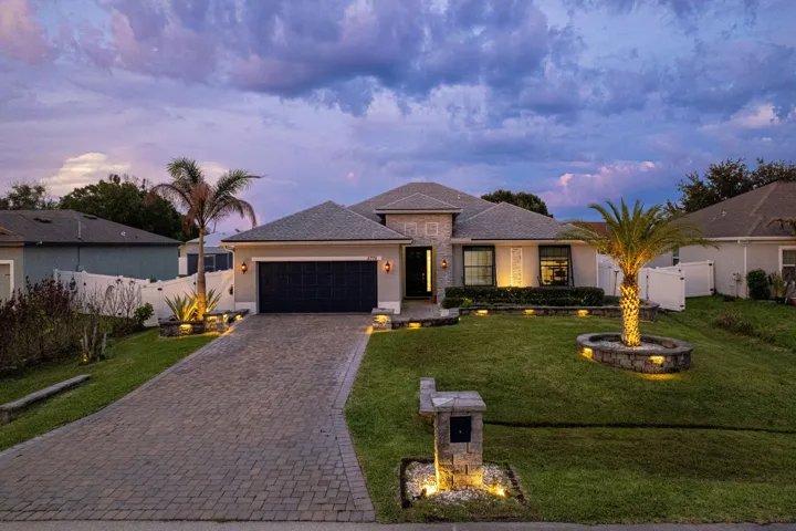 Paver driveway, stone-clad facade accents, integrated landscape lighting, a privacy fence, and a stone-clad planter