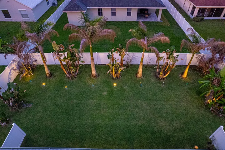 Expansive lawn with mature palm trees, perimeter fencing, and integrated landscape lighting