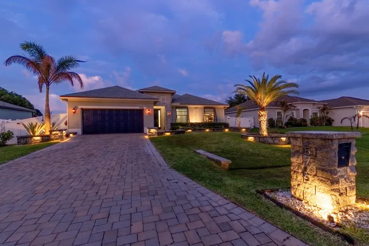 Paver driveway, integrated landscaping, mature palm trees, stone veneer accents, and exterior lighting