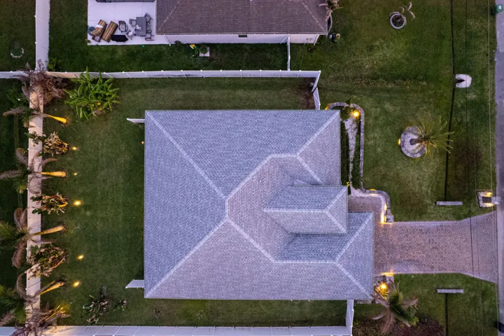 Paved driveway and walkways, mature palm trees, perimeter fencing, and exterior landscape lighting