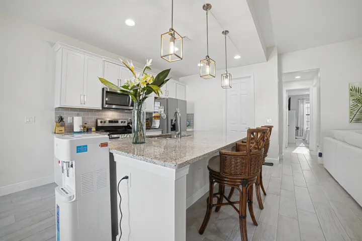 Kitchen featuring white cabinetry, stainless steel appliances, a tile backsplash, granite-finish countertops, and three pendant light fixtures