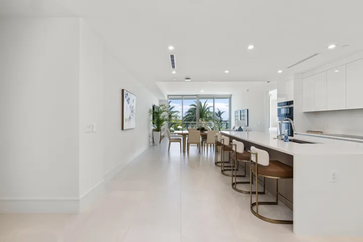 Contemporary open concept living area with light-toned flooring, recessed lighting, expansive floor-to-ceiling windows, and a kitchen island with integrated seating