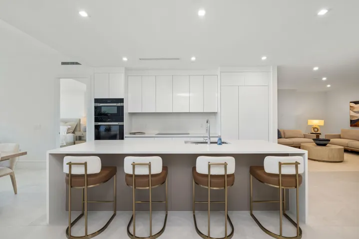 Spacious kitchen island with an integrated sink and light-toned countertop, built-in double ovens, and white flat-panel cabinetry