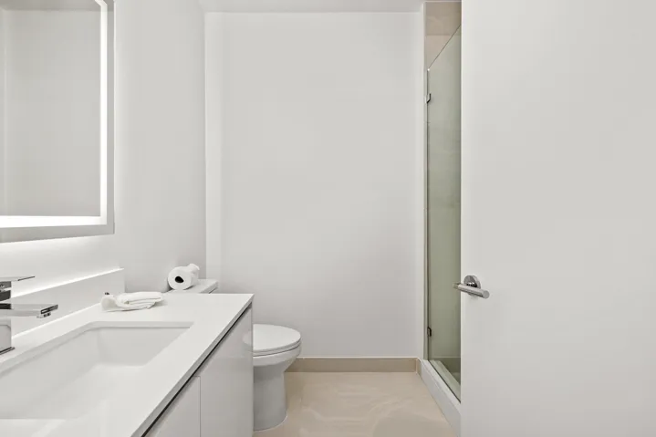 Modern vanity with integrated sink, chrome faucet, illuminated mirror, and glass-enclosed shower