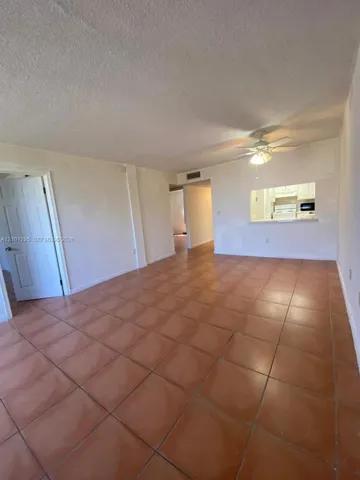 Ceramic tile flooring, white interior walls, ceiling-mounted light fixture with fan, and a kitchen pass-through window with counter ledge