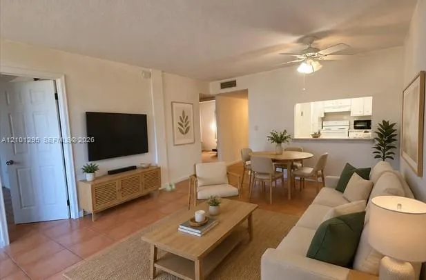 Open-concept living space featuring ceramic tile flooring, a neutral color palette, a ceiling fan with integrated lighting, and a passthrough opening to the kitchen