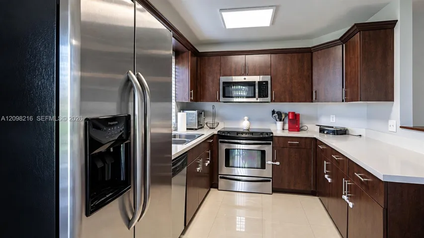 Kitchen with stainless steel appliances, rich espresso cabinetry and light countertops.