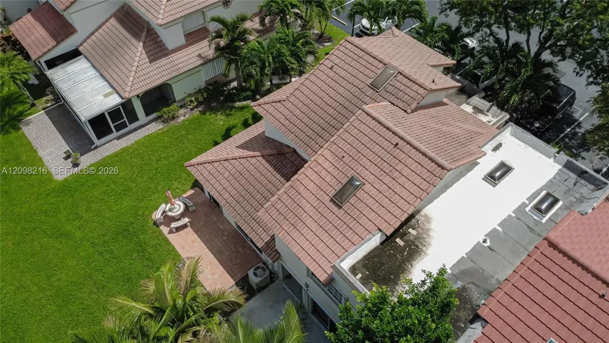 Aerial view of the home and its tile roof, surrounded by mature landscaping and green space.
