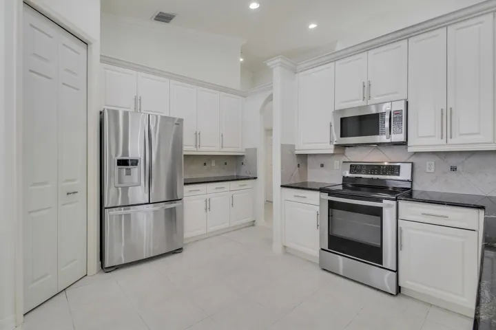 Bright kitchen featuring white cabinetry, stainless steel appliances, dark countertops, and tile backsplash