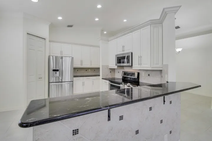 Kitchen featuring white cabinetry, stainless steel appliances, dark stone countertops, tile backsplash, and recessed lighting