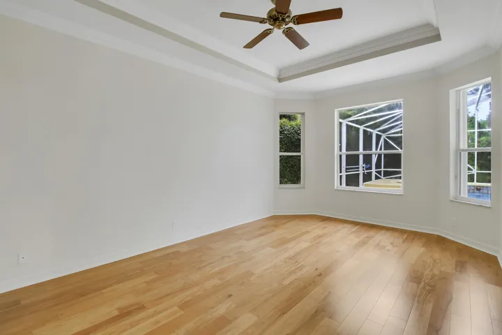 Wood-finish flooring with multiple windows, a tray ceiling, and a ceiling fan