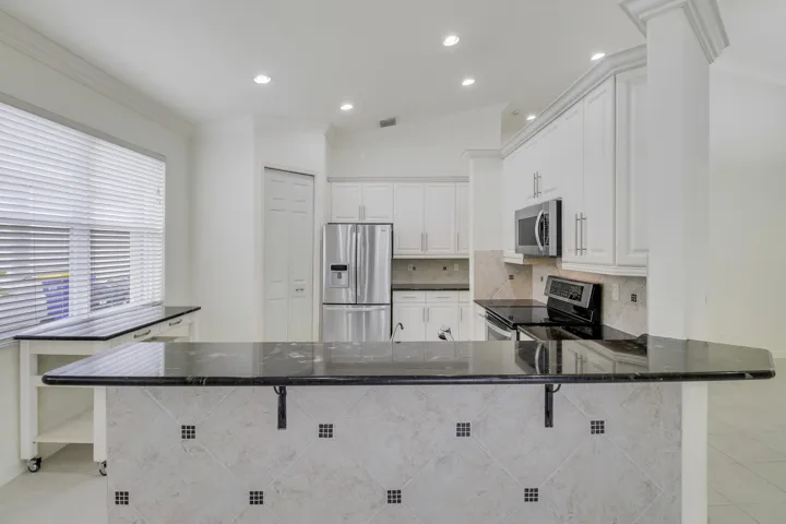 Kitchen featuring white cabinetry, dark stone countertops, stainless steel appliances, and a tiled breakfast bar