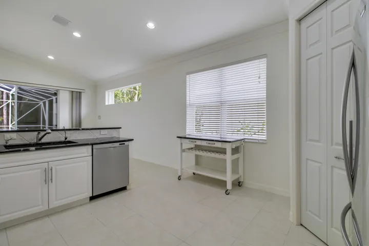 White shaker-style cabinetry with dark countertops, stainless steel dishwasher, tile flooring, and recessed lighting