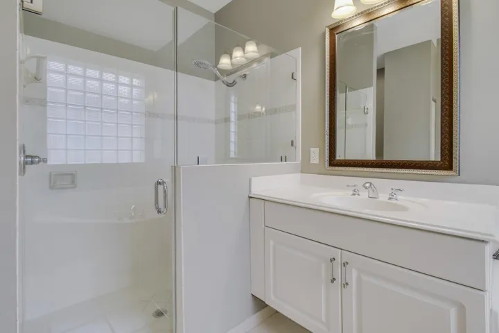 Glass-enclosed shower with a block glass window, single vanity with a white countertop and integrated sink, and an ornate framed mirror
