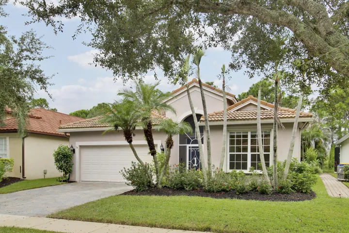 Mediterranean-style exterior with a tile roof, arched entryway, and mature landscaping