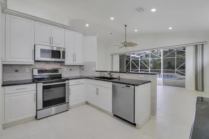 White cabinetry with crown molding, stainless steel appliances, dark stone countertops, and a tile backsplash