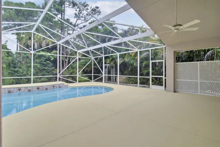 Screened enclosure featuring a freeform pool and spa, concrete decking, and a covered patio with a ceiling fan