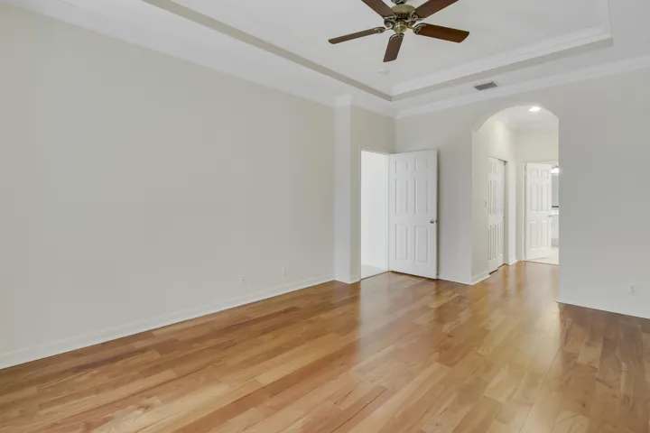 Hardwood flooring, tray ceiling with crown molding, ceiling fan, white paneled doors, and arched doorway