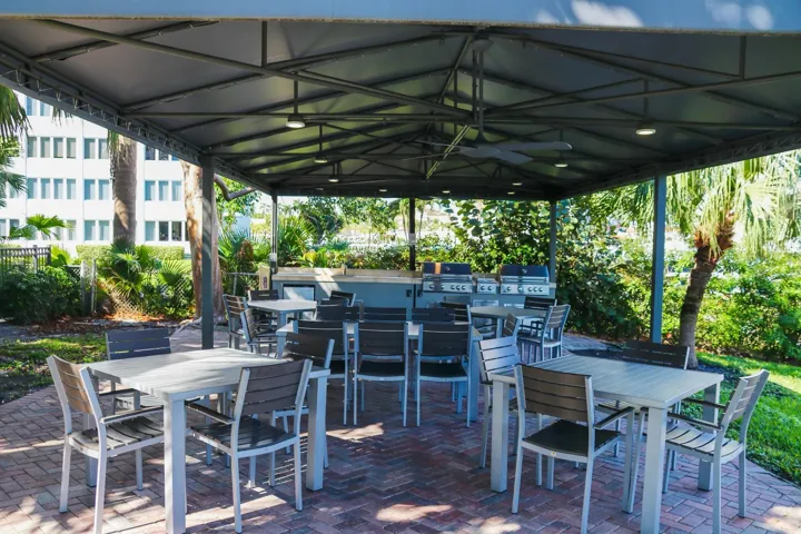 Covered outdoor patio featuring a brick paver base, integrated ceiling lights, and an outdoor kitchen with multiple grills