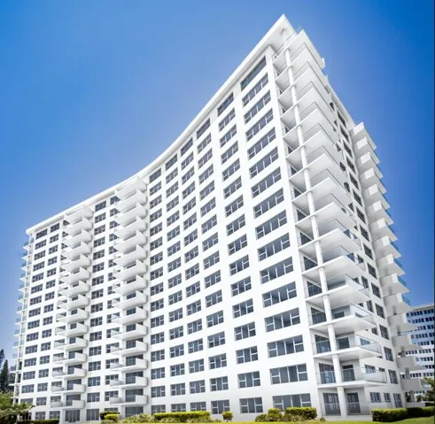 Curved architectural design, white exterior finish, extensive glazing, multiple private balconies with glass railings, and ground-level landscaping