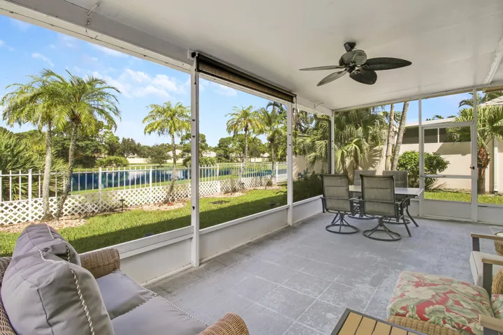 Screened patio with a ceiling fan, offering an expansive lawn and mature palm trees