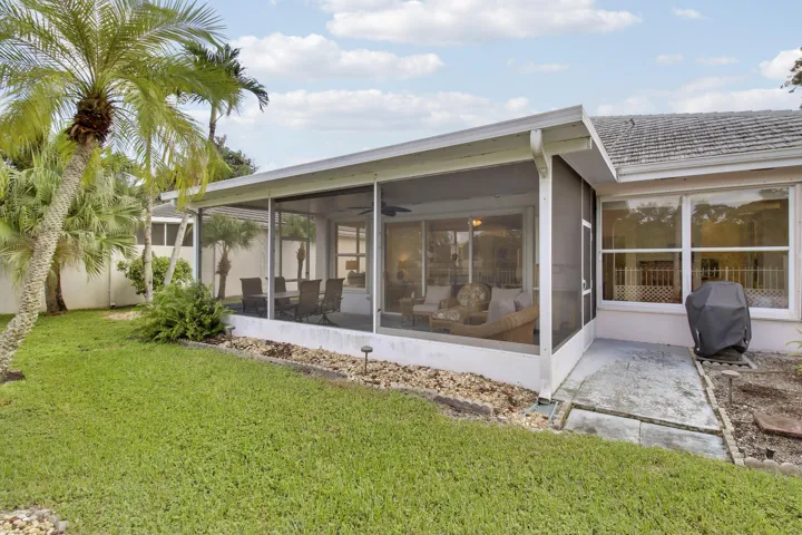 Screened lanai, expansive window panels, concrete patio, mature landscaping, and a manicured lawn