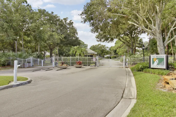 Gated entry with a guardhouse, double white metal gates, and a community sign