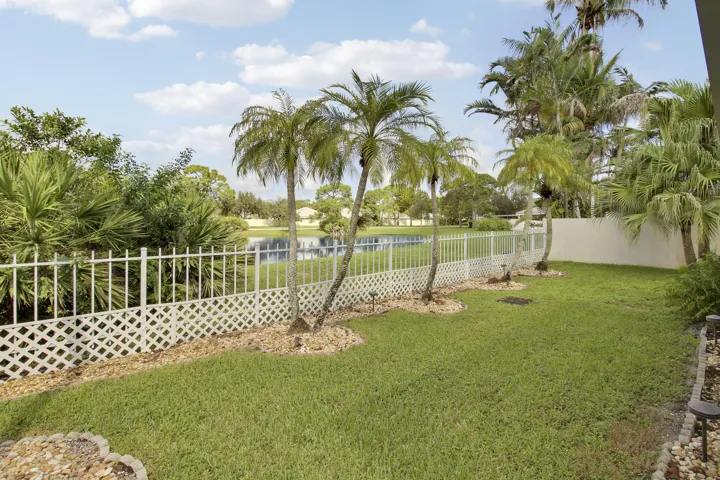 Expansive green lawn with mature palm trees, bordered by a white lattice and picket fence