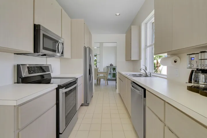 Galley kitchen featuring light-toned cabinetry, stainless steel appliances, a window above the sink, and tile flooring