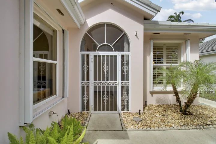 Arched entry with decorative security door, accordion shutters, and landscaped front yard.